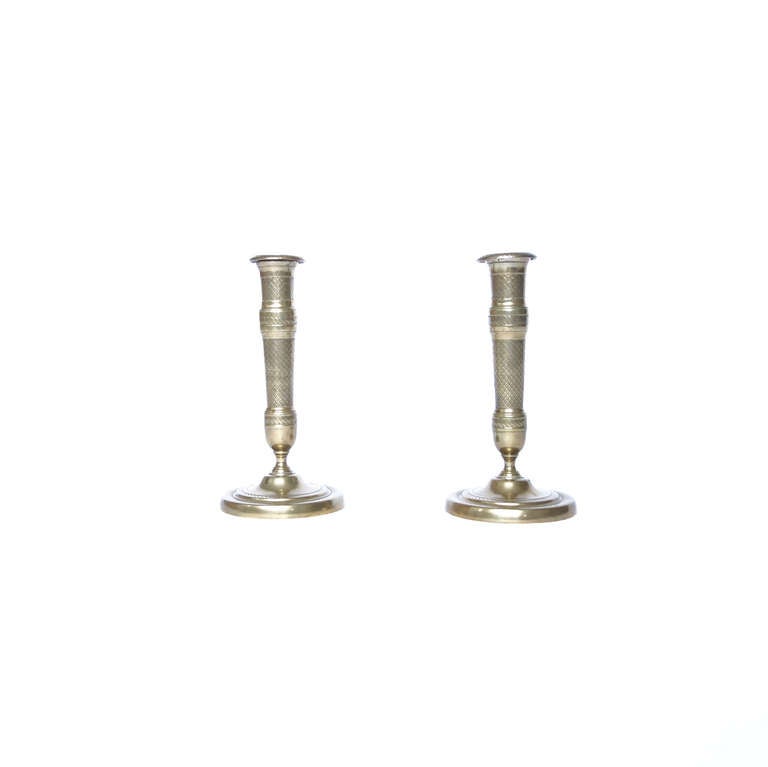 A fine pair of engine-turned brass candlesticks from the early 19th century. The patterns impressed in the bands alternate between beaded rows and diamonds and smooth brass, a restrained composition relative to other examples of the same period. We