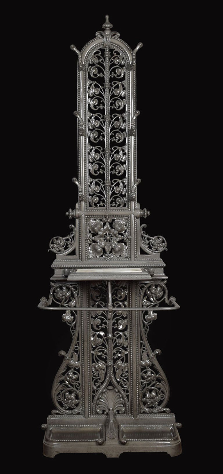 Victorian cast iron hall stand, the pierced scrolling leaf cast back  flanked by six scrolling coat hooks, the lower section with cast iron shaped bar to receive sticks and umbrella with detachable cast iron two handled drip tray, on shaped