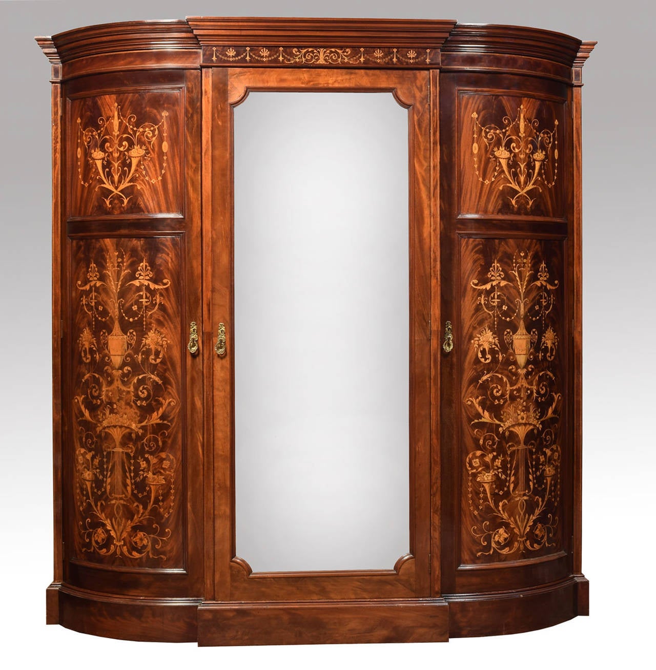 Early 20th century mahogany and marquetry triple wardrobe retailed by Maple & Co. Ltd London and Paris, having moulded cornice above the central bevelled mirror door opening to reveal and arrangement of sliding trays and short drawers flanked by a