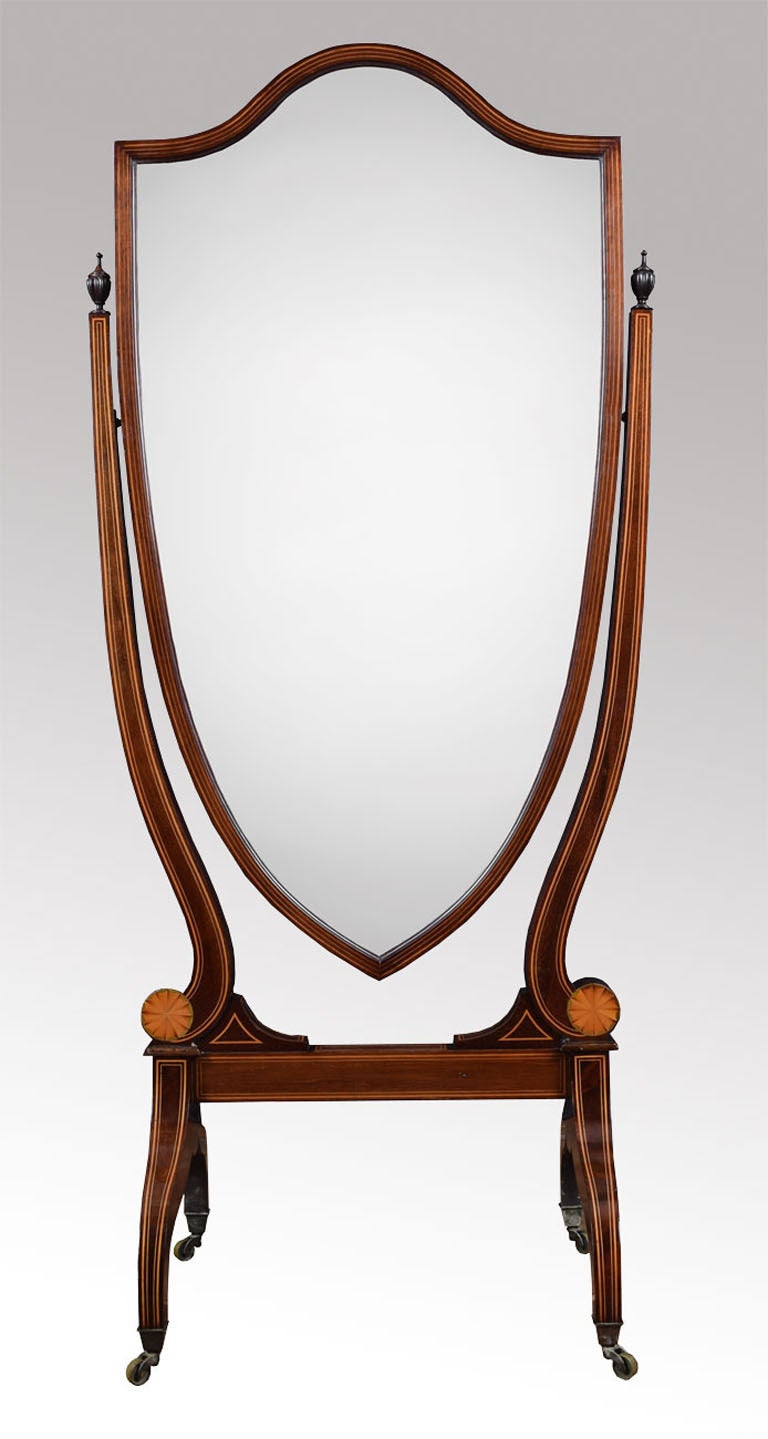Mahogany inlaid Edwardian cheval or dressing mirror. Having a shield-shaped bevelled mirror with line inlay, supported on lyre ends carved mahogany finials and shell inlaid paterae. The whole supported on swept mahogany supports with brass cup
