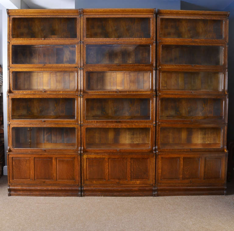 Three large solid oak six sectional bookcases the shaped cornice above five graduated tiers and lift up glazed doors above a panelled door section raised up on shaped plinths
