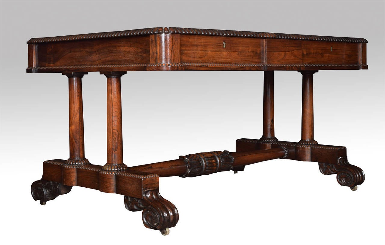 Rosewood writing table, the rectangular top over two panelled frieze drawers, with faux draws to the opposing side on twin circular turned end supports, platform base with scrolling feet terminating in brass castors.

Dimensions:

Height 29