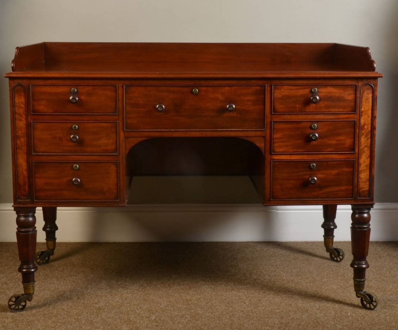 Mahogany tray top dressing or writing table, the rectangular top with raised three quarter gallery above the central shallow frieze drawer over an arch kneehole and flanked on either side by three short drawers, raised on blustered and fluted
