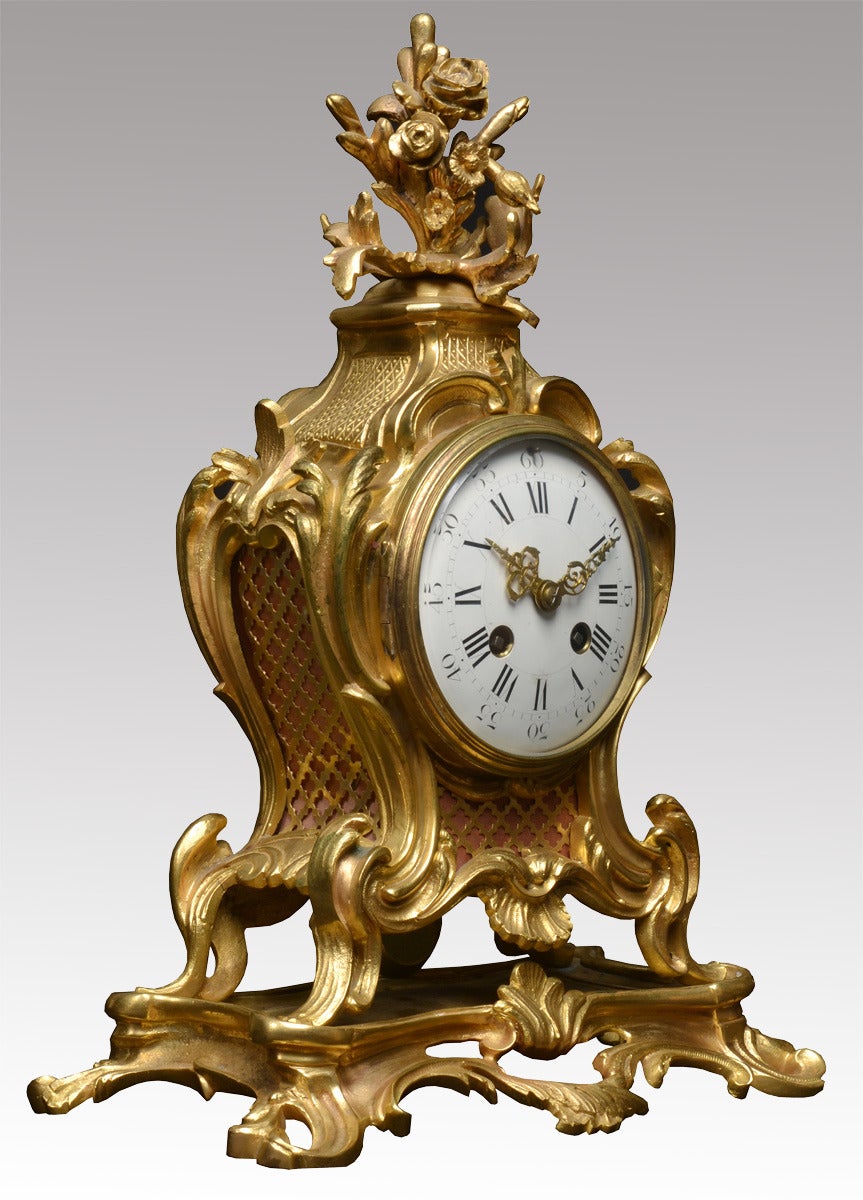 Three piece gilt metal clock garniture set, the Rococo style clock having scroll leaf and shell decoration and having a white enamel dial with eight day French striking movement by A D Mougin and having a pair of flanking four branch candelabras