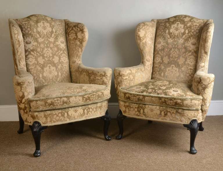 Pair of George I style wing armchairs having ebonised front shell carved cabriole legs, with swept legs to the rear upholstered in damask upholstery having removable cushion.