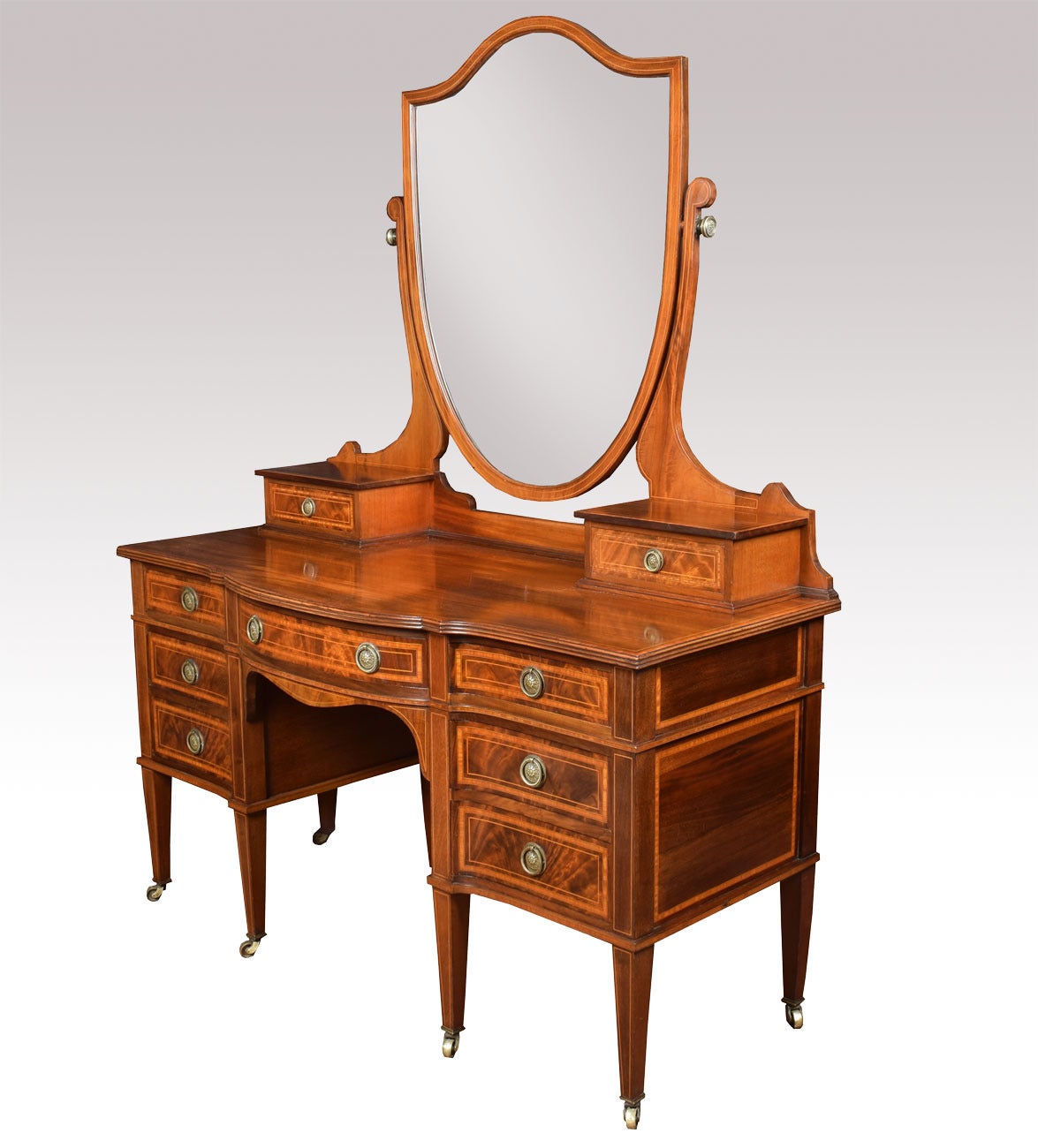 Edwardian mahogany dressing table by Maple & Co. the shield shaped mirror Flanked by one short draw to each side above figured mahogany top. The base section fitted with central draw having brass tooled handles with three further draws to either