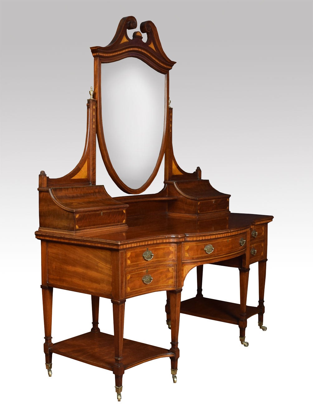 Edwardian Mahogany dressing table , the Shield Shaped inlaid Mirror Flanked by lidded comartments to each side above figured mahogany top. The base section fitted with central draw having brass tooled handles with two further draws to either side