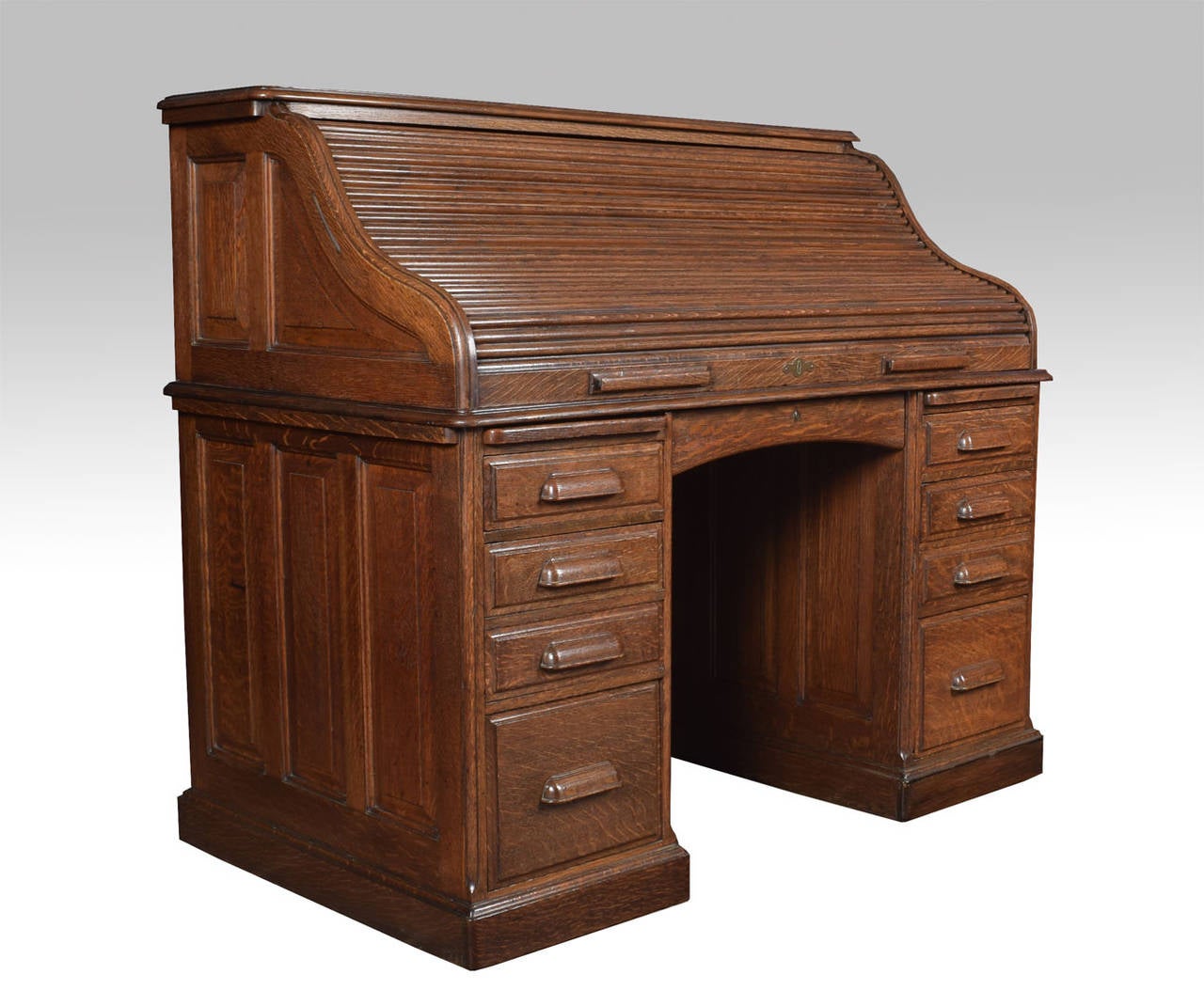 Oak double pedestal roll-top desk, the high back with fully fitted interior of pigeon holes and drawers, the centre drawer flanked by pedestals having brush in slide above three short draws and one double draw raise up on plinth base

Height 54