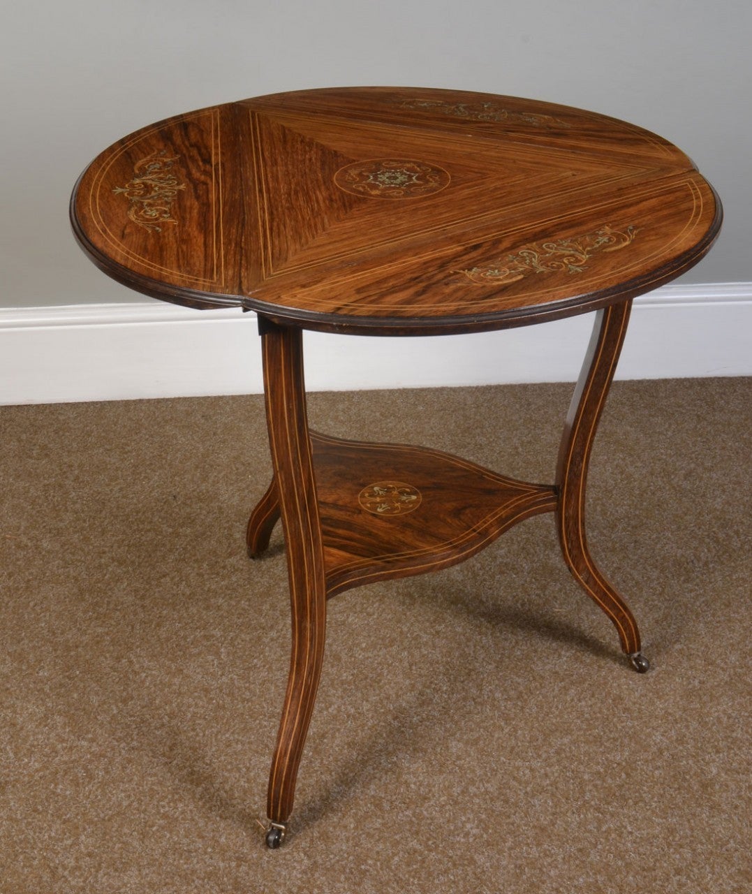 Rosewood inlaid triangular occasional table having three drop flaps inlaid with floral design and ivory flowers above shaped turned legs united by under tier  raised up on brass castors
Dimensions
Height 27.5 Inches
Width 22.5 Inches