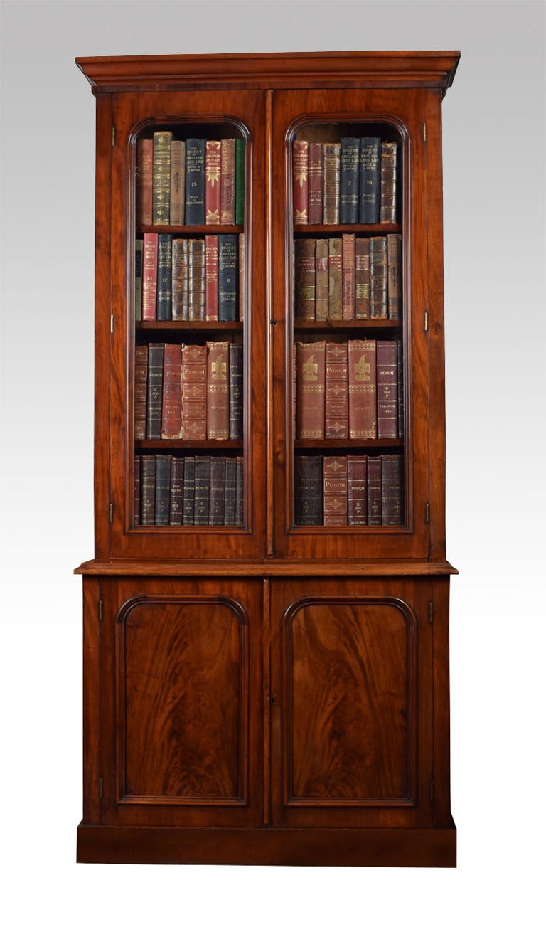 Victorian mahogany bookcase with a flared cornice over two glazed arched doors enclosing three adjustable shelves, the protruding base having two flame mahogany panelled doors opening to reveal single fixed shelf raised up on plinth