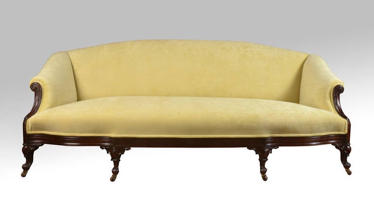 George II style mahogany serpentine sofa, with an arched padded back and scrolled arms recently upholstered, on fluted scrolled cabriole legs carved with foliage and C-scrolls, terminating in brass ceramic castors in the manner of Paul Saunders