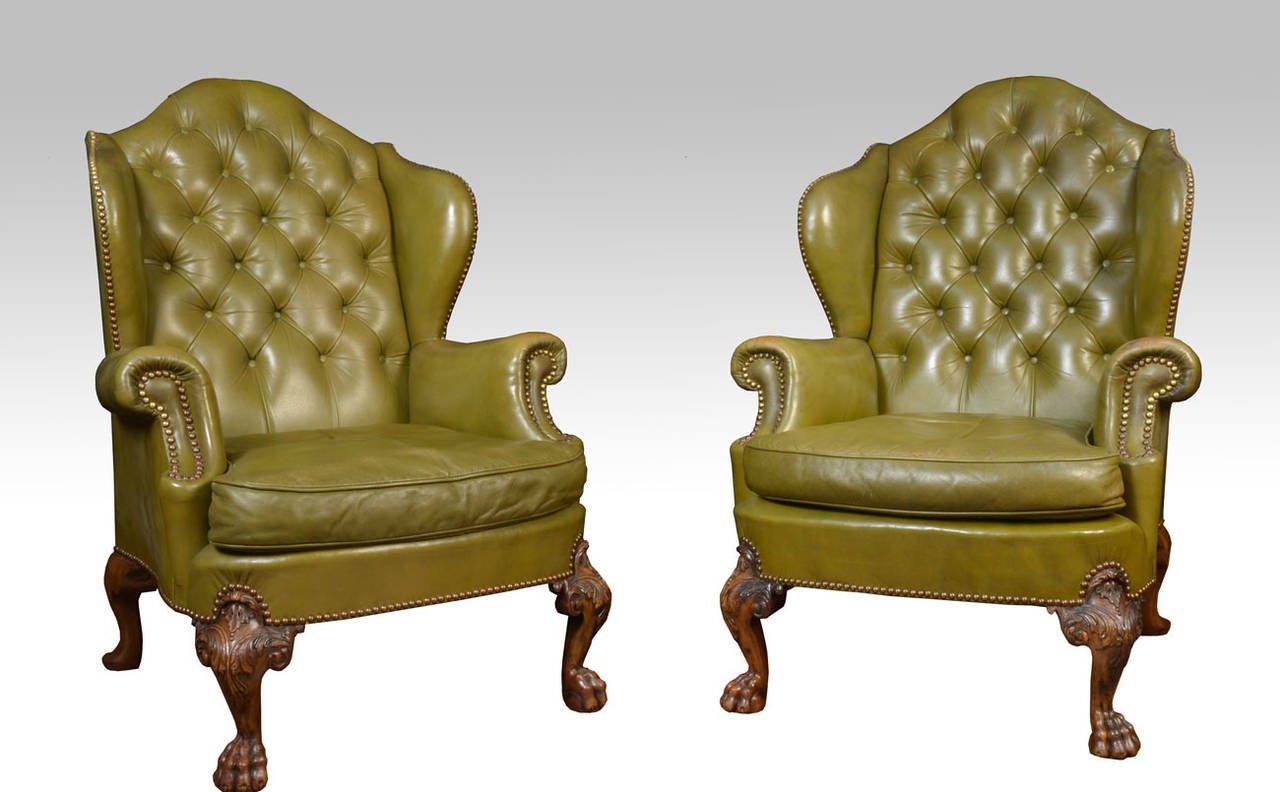 Pair of wing armchairs in George II style, with olive leather upholstered sides, back and seat, on walnut leaf carved cabriole legs with claw and ball feet