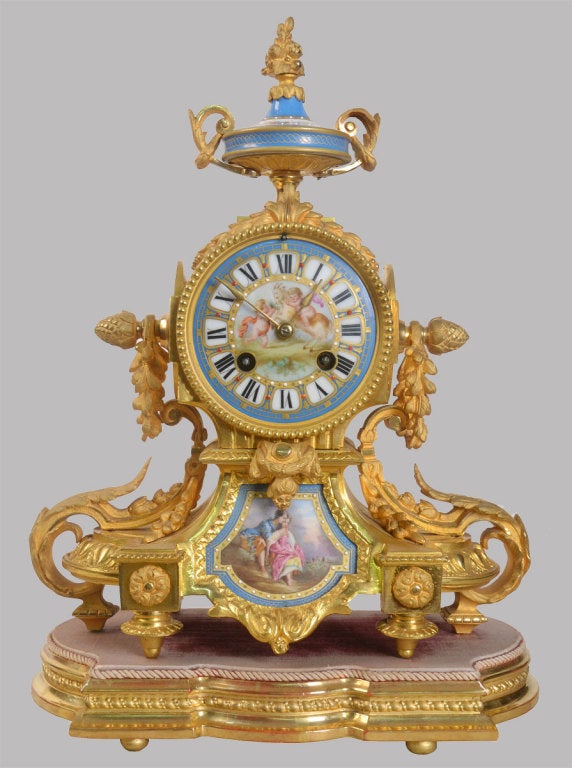 French ormolu cased mantel clock decorated with floral sprays, masks floral painted porcelain plaques and urn finial, the movement by Japy Freres, the blue porcellain dial having Roman Numerals raised up on giltwood base