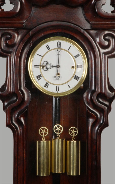mahogany cased, with brass triple-weight driven time and strike movement, having two-part enamelled dial. The Art Nouveau mahogany case with carved pediment and shaped three glass case.