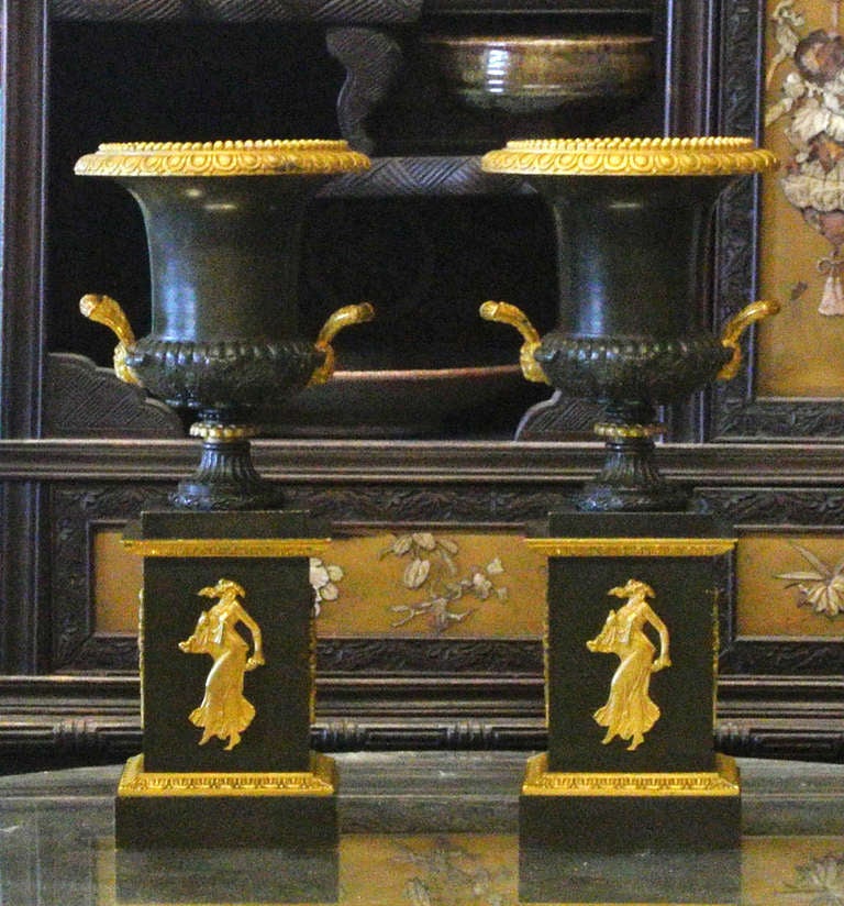 A nice pair of French Neoclassical bronze and gilt urns. Each with a rich dark green patina. The handles feature well formed lion heads. The two side panels with a sheaved harvest bouquet. The front with a dancing maiden throwing flowers from a