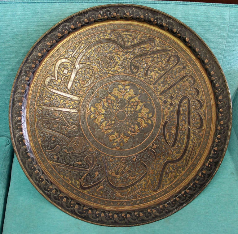 An unusual tray, round in form with rolled edge rim. The outer border with an interlocking fish motif. The interior decorated with large calligraphic medallions in Thuluth script and intertwining arabesques.  The center with floral arabesques and