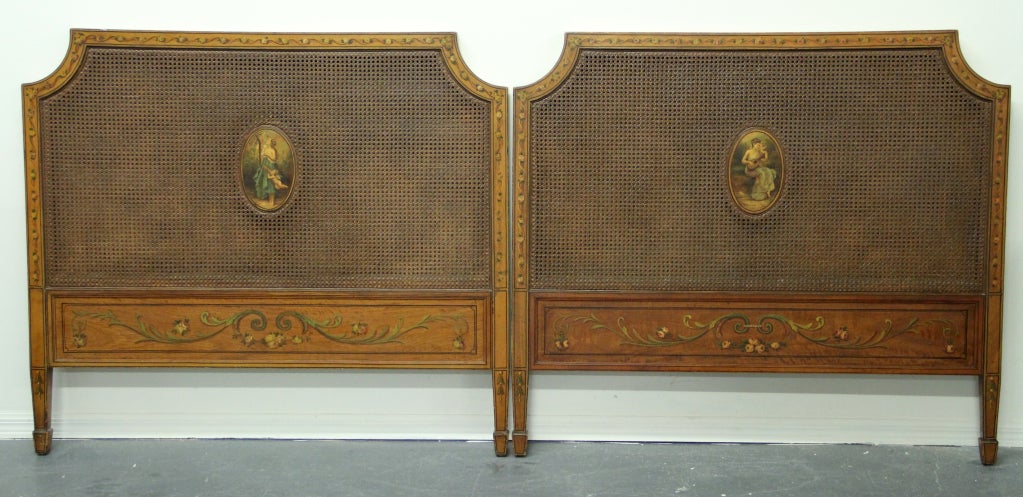 A rare pair of George III style painted satinwood twin beds in the style of English Cabinet maker, George Seddon. The head and foot boards feature caned insets with exquisitely painted center medallions, and floral borders. George Seddon, Sons &