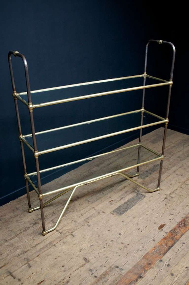 A tubular steel and brass shelving unit with three glass shelves.
Circa 1950.