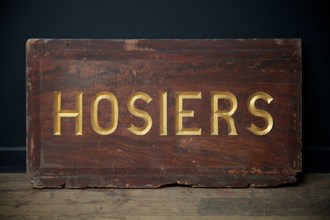 A hosiers chisel cut, gilded a faux wood grain painted softwood trade sign. 

English 1920s.