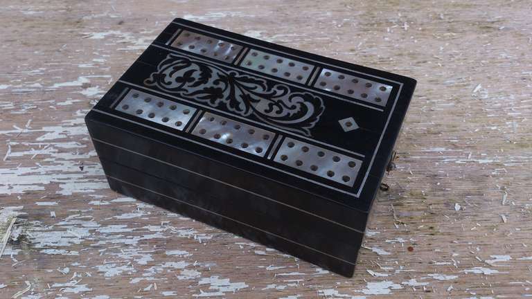 Folding Traveling Cribbage Board made of ebony with extensive mother of pearl contrafoliate to the top and with pewter stringing around the sides.  The interior is lined with pale blue moire and matching paper. There are four ivory pegs and a new