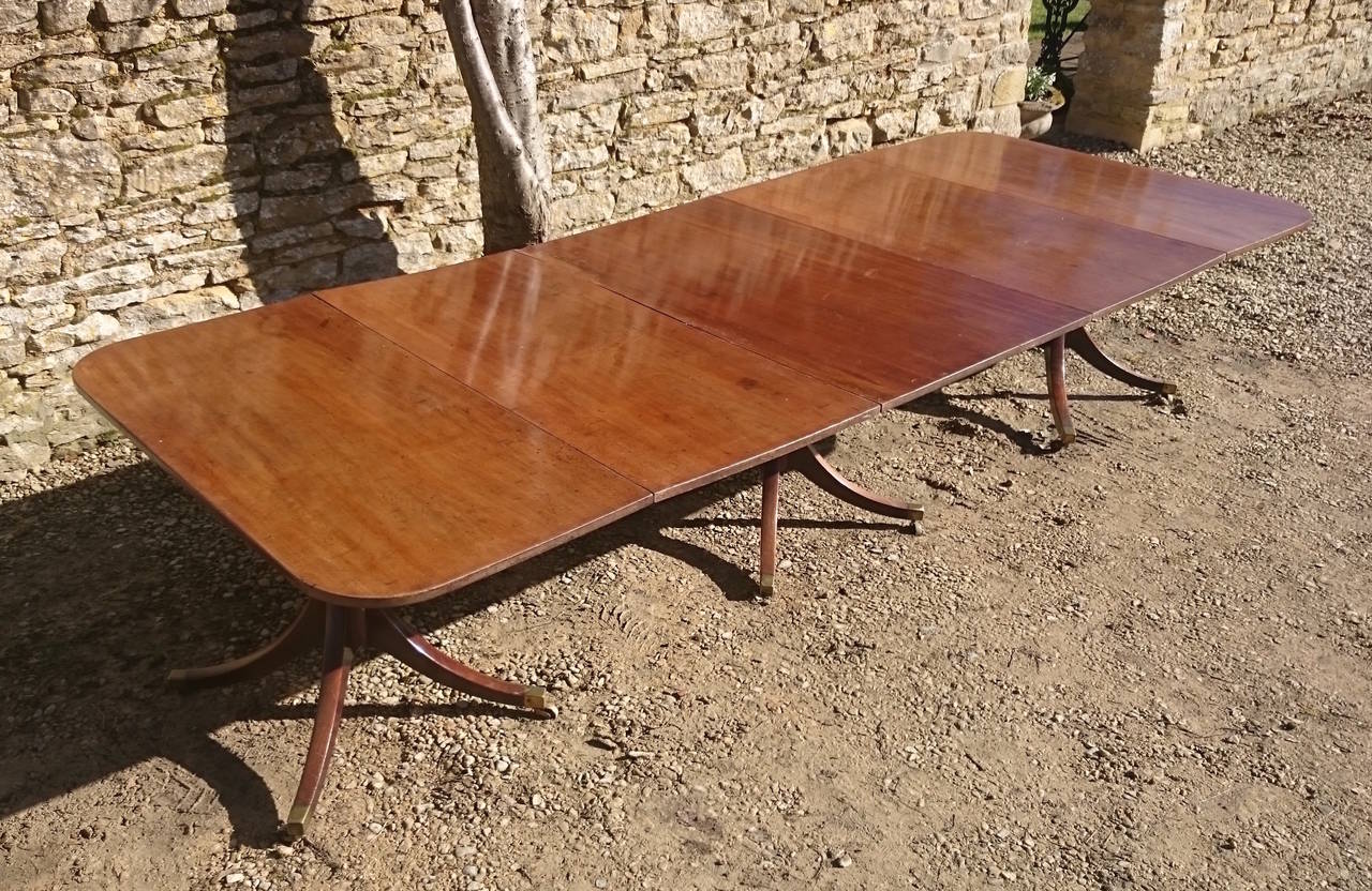 Antique three pillar dining table standing on four splay bases which terminate in brass cups and casters. This table is very good value for a table of this early period and quality. The large sheets of solid mahogany have an interesting grain