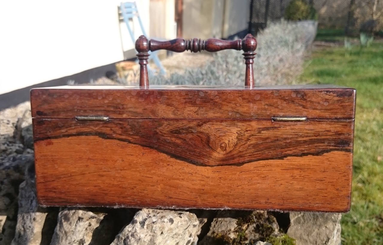 Antique pen and ink box made of rosewood unusually with turned fruitwood handle. The interior is made of rosewood and contains a pen tray, lidded compartment and two patent crown ink pots (Mosely pattern). There is a pull out drawer to the side.