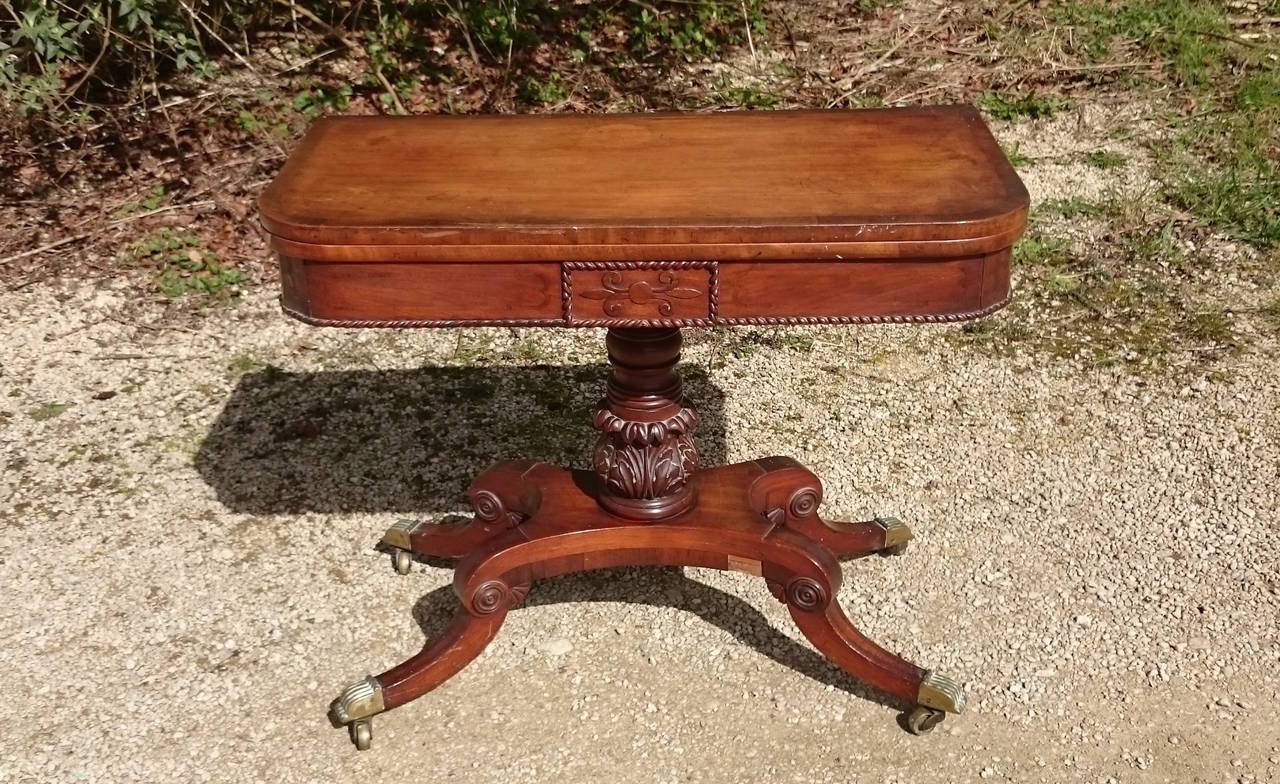 This antique card table is a fine example from the beginning of the 19th century. It is made of mahogany, is cross banded around the top, has gadrooned decoration all around and ebonised inlay to the frieze. The base is a slender column which