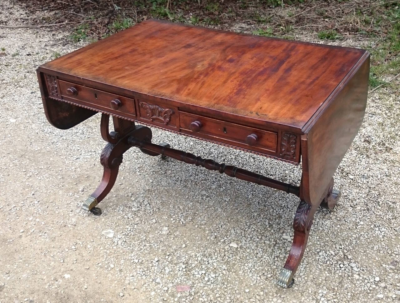 Antique sofa table made of finely figured mahogany with inlay and carving. This table stands on end supports with an elegant version of the Regency knee. The turned stretcher is thin and the carving is detailed. There are drawers one side and false