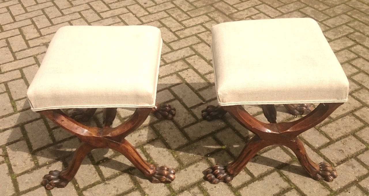 Pair of antique stools standing on x-frame bases with lions paw feet. They are made of walnut and have an especially generous shape to the legs. 

English circa 1860 

16