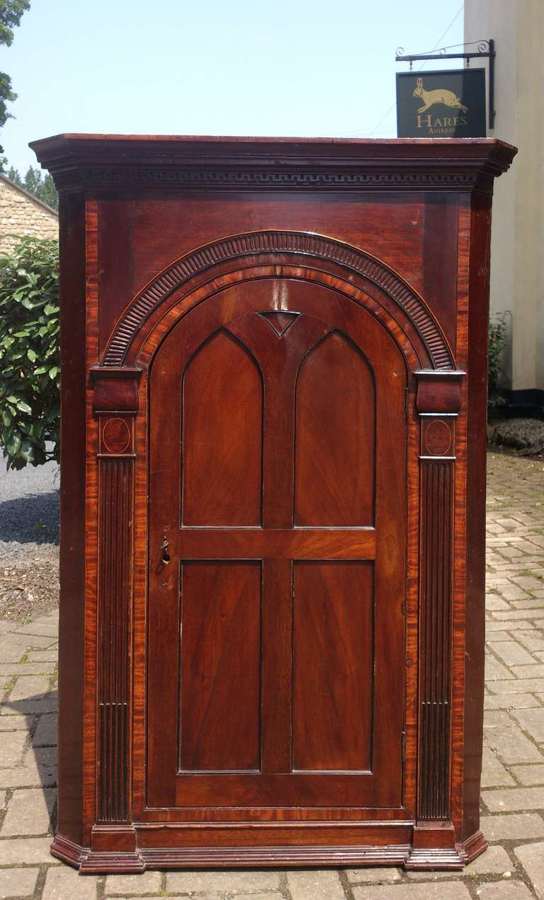George III period hanging corner cupboard made of mahogany with stringing and architectural decoration, arch to top of door, fluted pillasters either side of the door and dentil cornice at the top. English circa 1790 

17 1/2