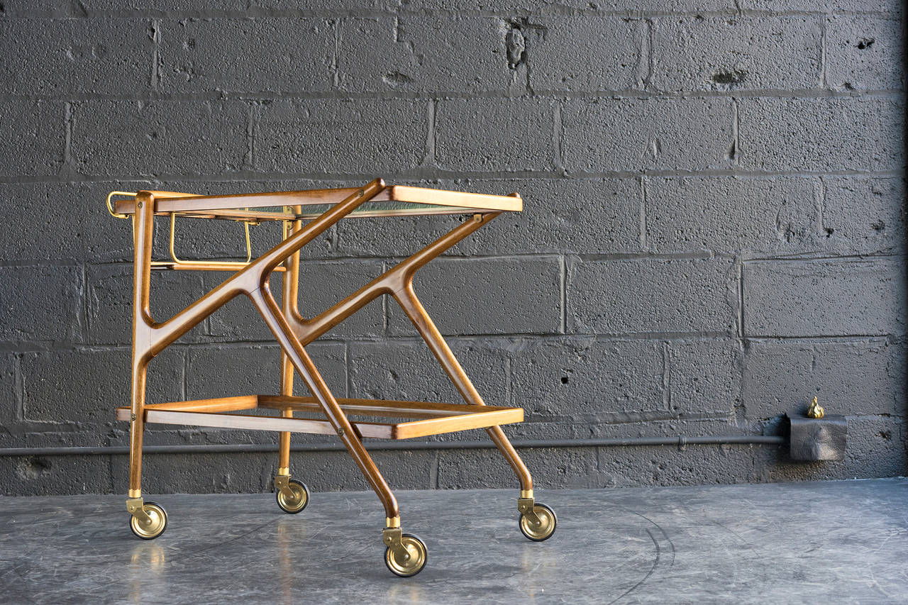 Charming double-k form. Warm, sculpted wood frame with brass hardware. Smooth rolling casters.