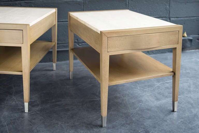Bleached mahogany tables with travertine top, single bombé drawer, lower shelf, and gently tapering legs ending in nickel sabots.

With their finished backs, these tables are presentable from every angle.