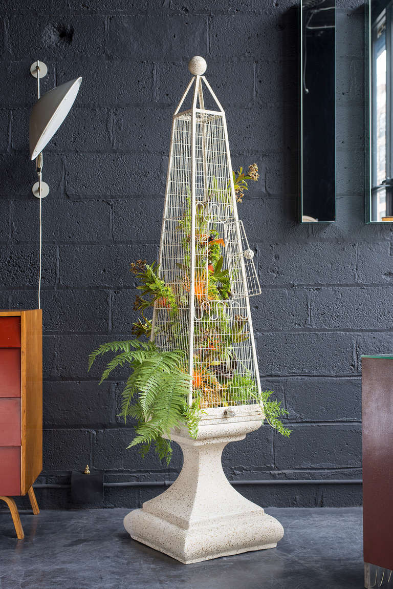 Available with or without the original flora & fauna installation. Obelisk form cage rests on flared plaster pedestal. Original off-white painted surface with gold speckles.