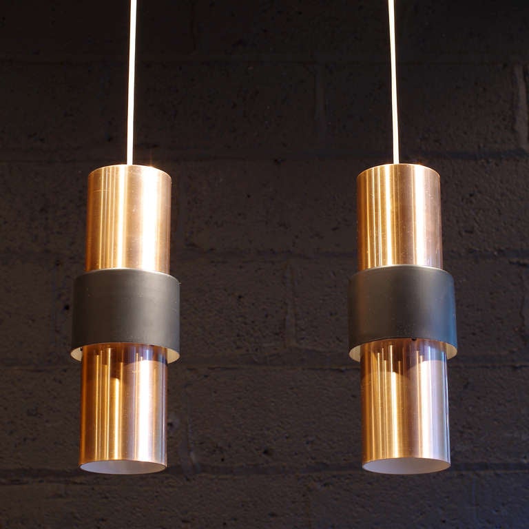 The outer matte black cylinder conceals a gap between the two rose colored cylinders from which light escapes, illuminating the sides of the pendant. The open bottom cylinder drops a pool of light to the surface below.

White electrical cord