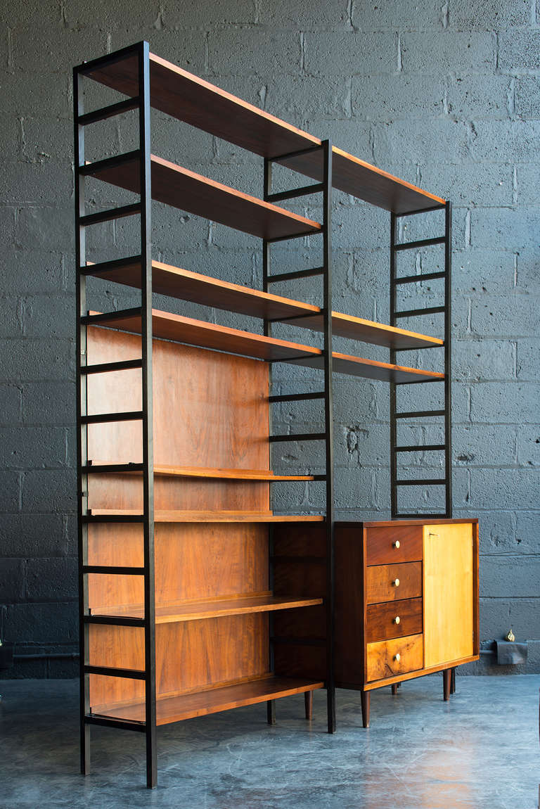 A rare & smart mid-century piece with eleven adjustable shelves, three black ladder-form vertical supports, two wood back panels, and one freestanding cabinet.

Mixed exotic wood construction with rich, warm tone. Original key. Original paper