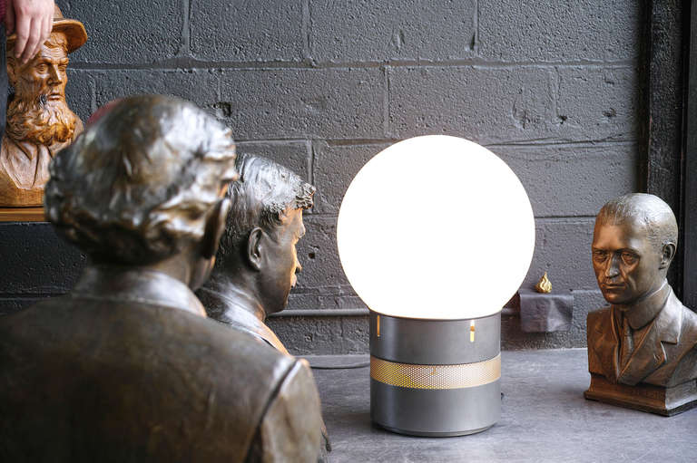 Table or floor lamp. Dimmer-controlled main light within large glass globe. Separately controlled night lights filtered through perforated metal band in base. Gray powder coated metal.