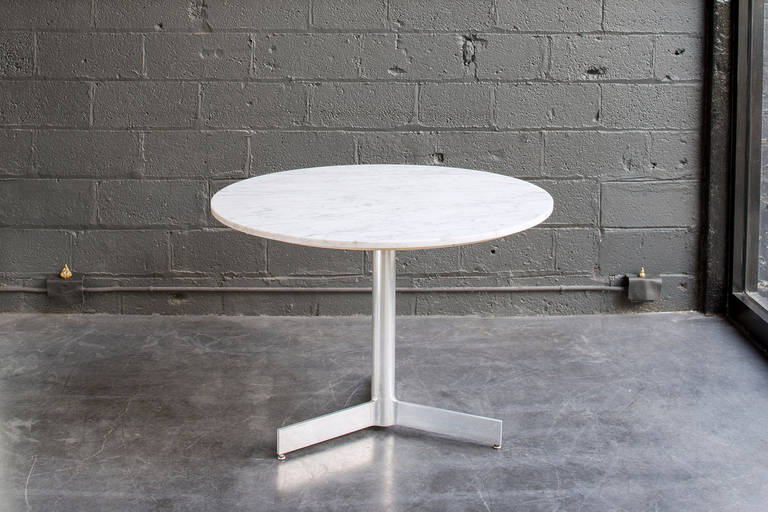 Understated form comprised of a honed carrera marble top on three-footed aluminum pedestal base with adjustable feet.