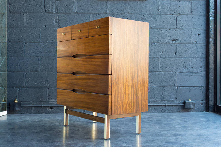 American modern dresser with seven drawers, recessed eye-form pulls, three original metal pulls, rich tone & figured grain, and inset wood legs with aluminum detail. Branded inside drawer.