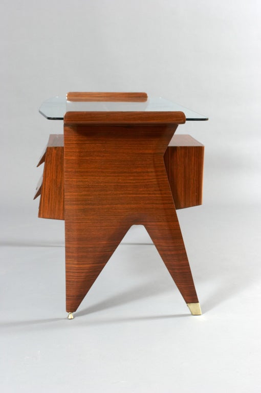 A small desk with angled glass top and sculptural mahogany base with two drawers and brass sabots. Desk is manufactured by Dassi. The desk has been authenticated by Ambrogio Dassi ( founder of Dassi) as being designed by Gio Ponti.  The desk was