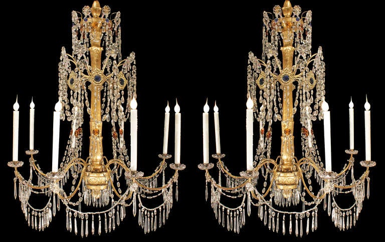 A spectacular pair of Italian 18th century giltwood, clear and colored glass, and crystal eight light Genovese chandeliers. Each elegant chandelier has a carved giltwood central fut with a bottom finial and kite shaped crystals. Each S scrolled gilt