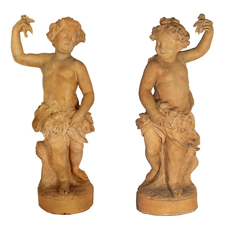 A pair of large scale French mid 18th century terra cotta statues. Each statue is raised on a circular base with fanciful frolicking putti in front of tree trunks. The putti each with a raised arm holding flowers, in classical drape decorated with