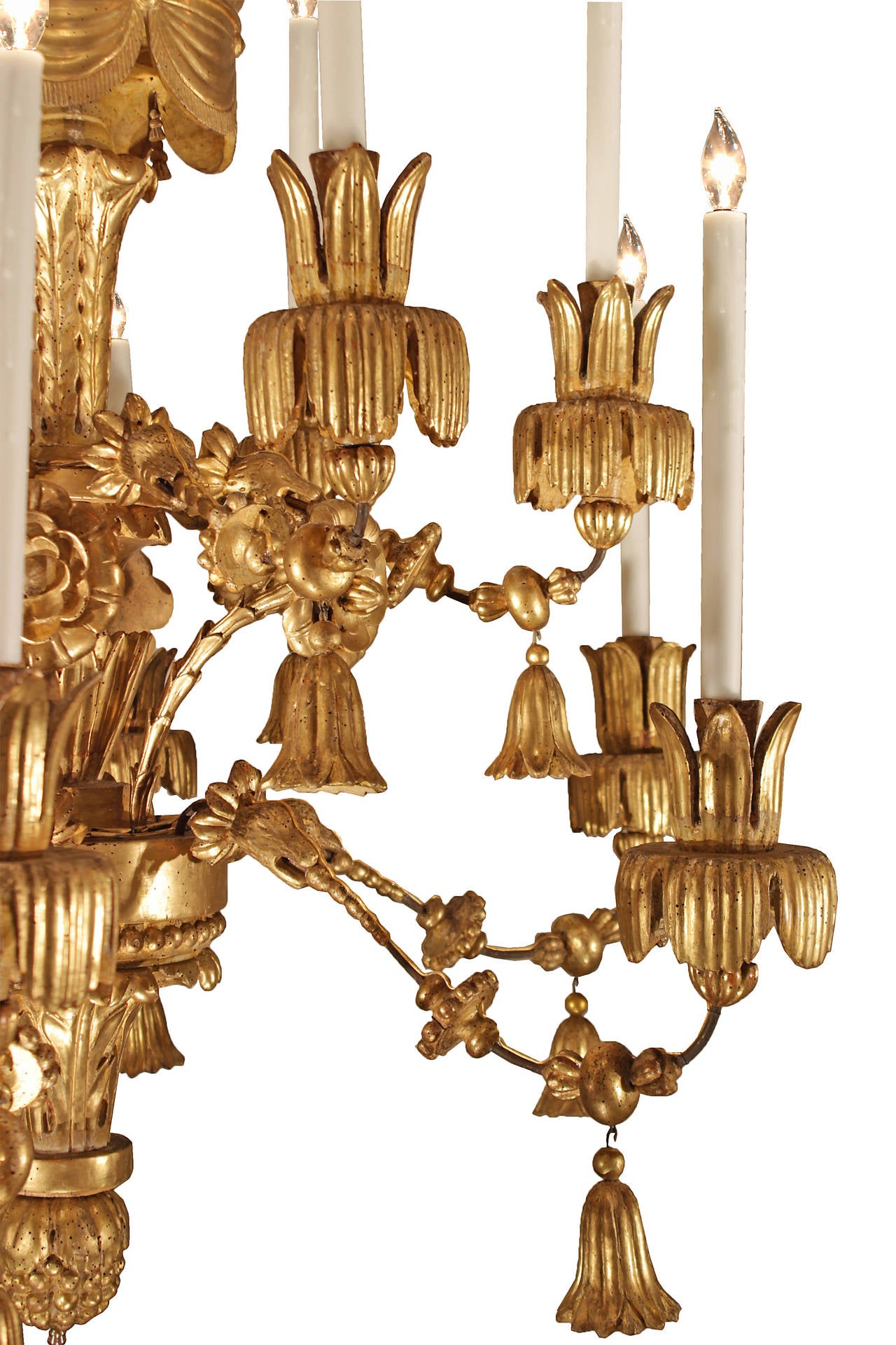 A stunning and large scale Italian early 18th century carved giltwood  twelve light chandelier circa 1730. The chandelier is centered by a carved bottom floral finial with a tassel pendant. The bottom tier of the central fut is decorated with richly