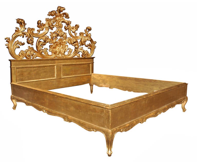A spectacular Italian 19th century Louis XV style giltwood bed. The bed frame is raised on short cabriole legs below the scrolled carved apron of the side and front boards. An impressive rectangular paneled head board supports a very impressive