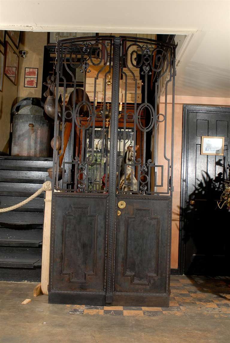 Pair of 19th century French iron doors with solid cast iron lower panels and grilles on the top portion with operable casement windows on the interior side, circa 1890.  This pair of doors has an elliptic arch at the top and are typical of French