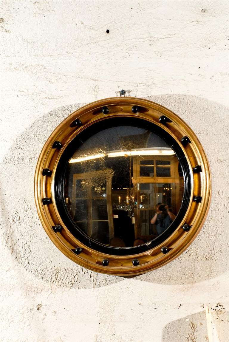 Late 19th century English gilded convex wall mirror with black ball decorations and trim framing the mirror, circa 1890.