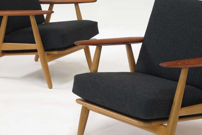 Pair of lounge chairs deigned by Hans Wegner for Getama circa 1955. 
Solid oak frame with teak arms, newly restored using period finishing techniques. Original inner spring cushions newly upholstered in a dark grey Scandinavian wool textile.