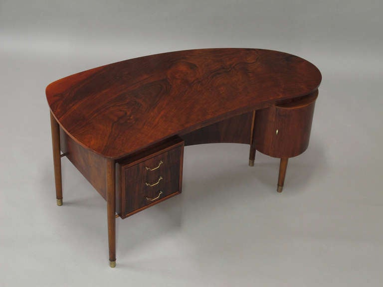 Danish Freestanding kidney shaped desk crafted of burled walnut with rosewood stain. Three drawers with brass pulls and circular cabinet. Finely finished back with open bookcase and cabinet. Tapered legs with brass caps.