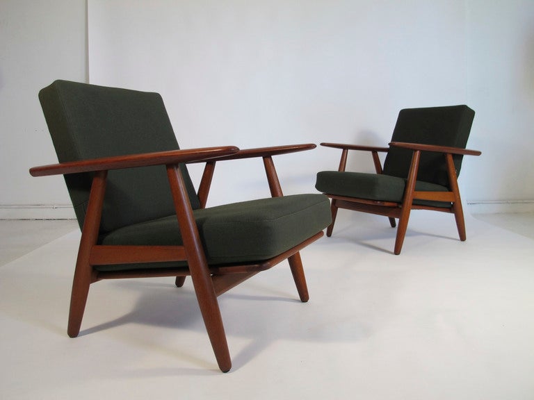 Pair of Hans Wegner designed cigar-arm lounge chairs in teak wood with green wool innerspring cushions. Slatted wood back, metal coil springs under the seat cushions. Manufactured by Getama c. 1955