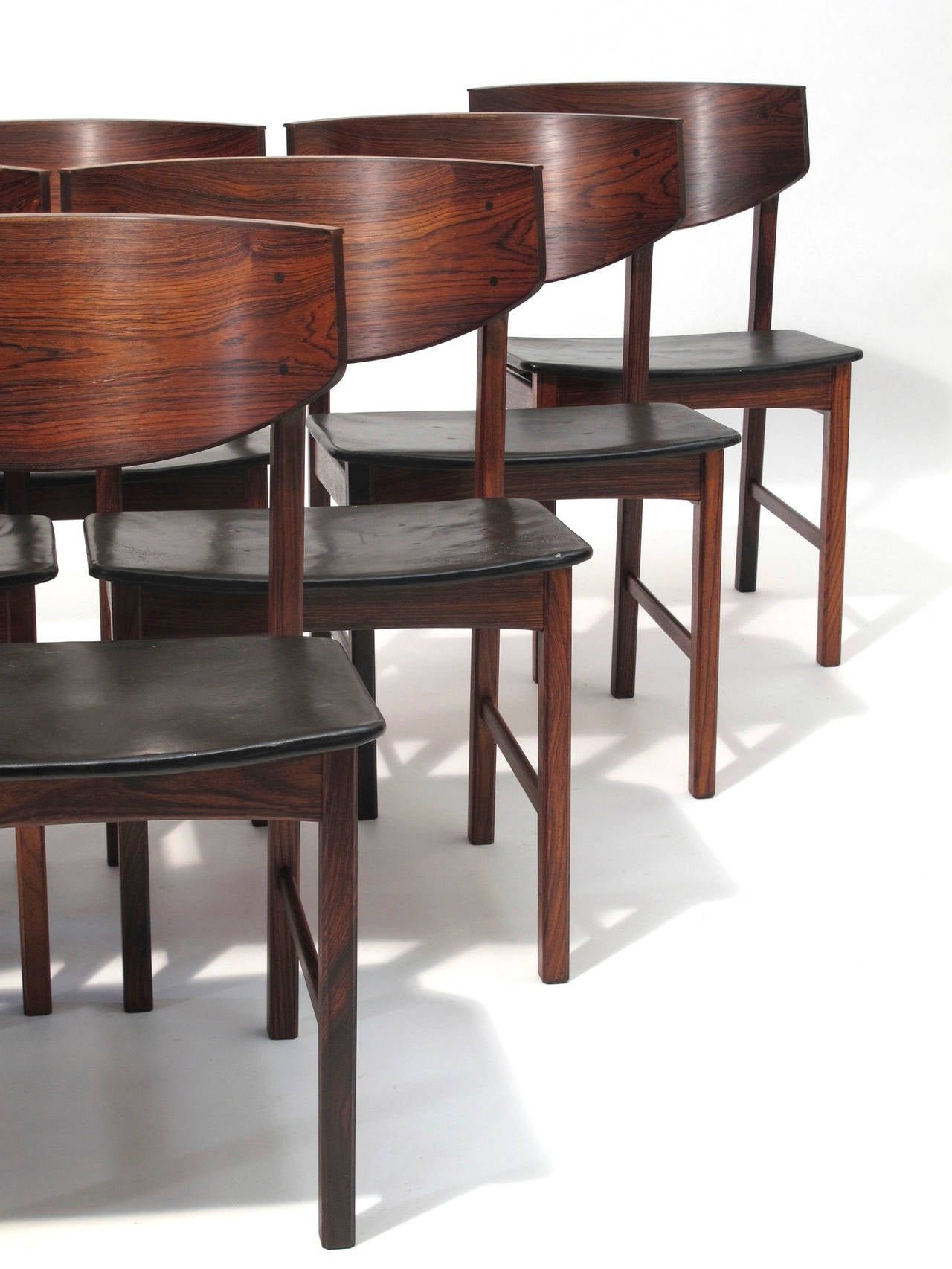 Eight Brazilian rosewood dining chairs with dramatic curved backs, rich dynamic grain and exposed joinery, upholstered in patinated black leather.