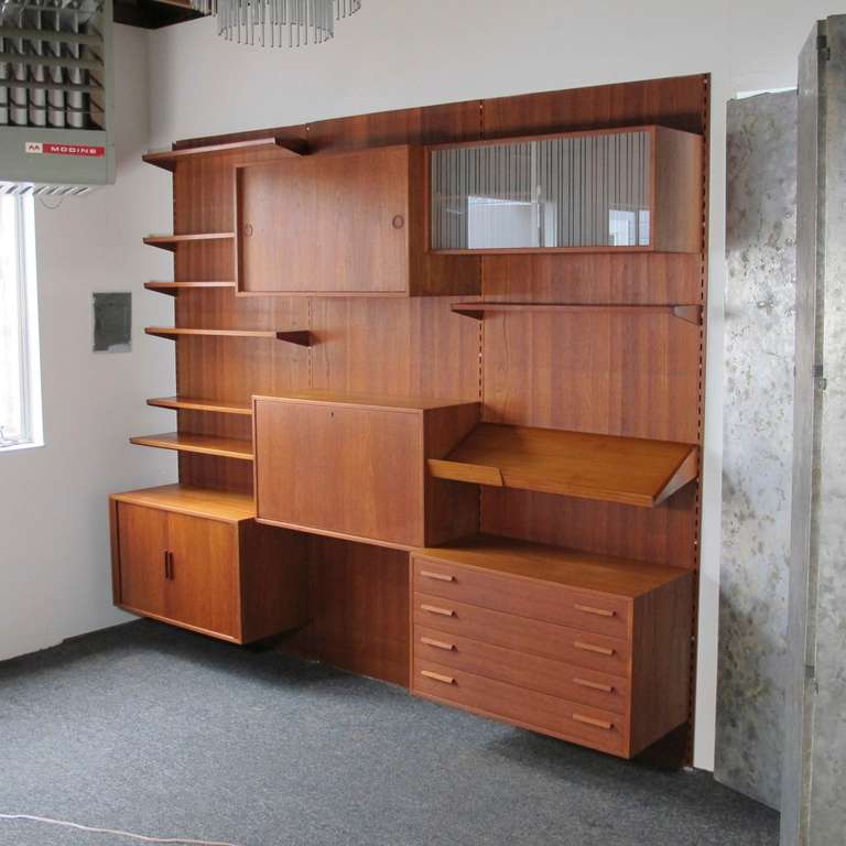Kai Kristiansen wall / shelf system in teak. Manufactured by FM Feldballe. Fully adjustable wall system includes:

8- teak shelves
1- cabinet with four drawers
1- drop front bar cabinet
1- cabinet with sliding doors and interior adjustable